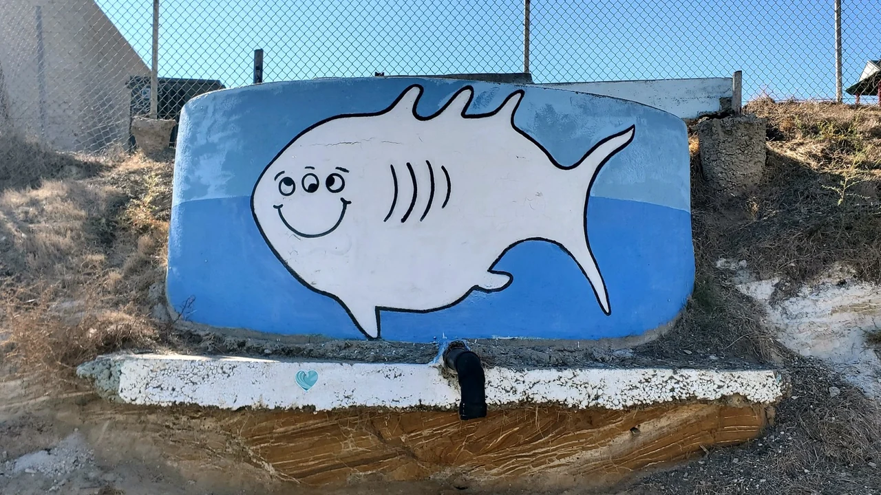White smiling three-eyed fish mural on blue concrete along Gaffey Street in San Pedro